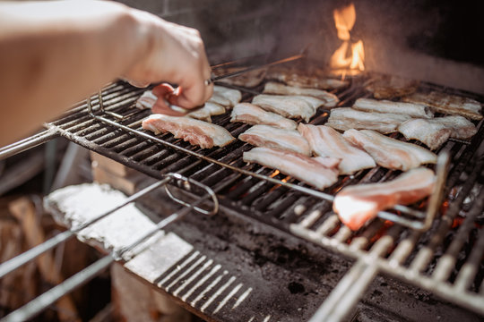 crop person cooking bacon in barbecue