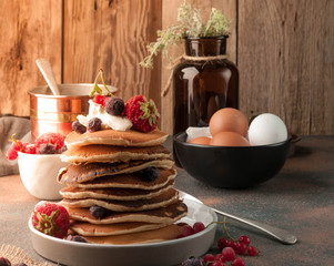 side view of stack of delicious brown traditional american pancakes with sour cream and fresh berries on table in white plate