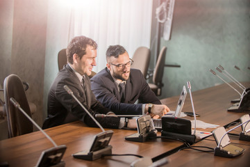  Image of two young businessmen discussing document in touchpad at   meeting