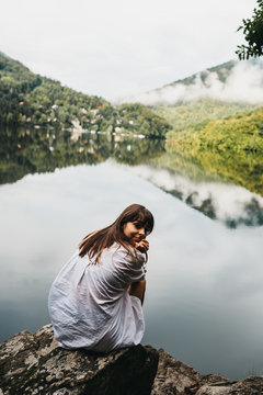 Woman sitting on rock near lake and mountains