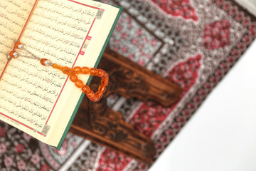 Islamic Holy Book Quran on wood carving rahle with rosary beads and prayer rug on isolated white background. Kuran the holy book of Muslims. Ramadan concept.