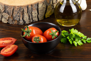 tomatoes in a black cup, olive oil and parsley on dark wood table