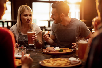 Young couple drinking beer and eating lunch with friends in a pub.