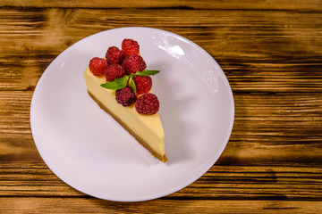 White plate with cheesecake New York, leaf of mint and raspberries on wooden table