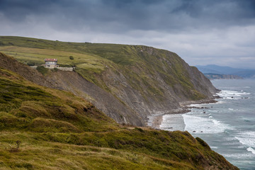 Scenic view over green hills, the lighthouse and ocean, waves hitting the rocks