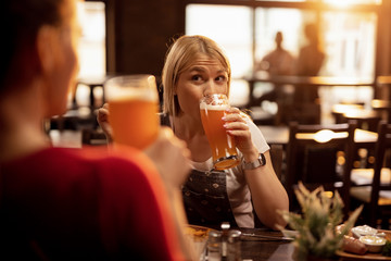 Young woman drinking beer while having lunch with a friend in a pub.