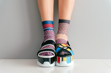 Beautiful female legs in mismatched trendy socks standing in two different fashionable high wedge...