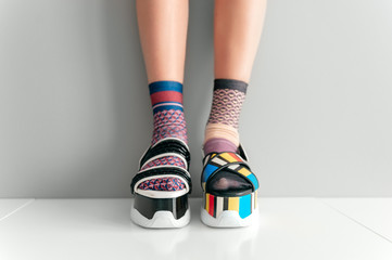 Beautiful female legs in mismatched trendy socks standing in two different fashionable high wedge...