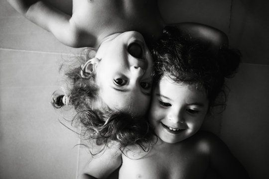 black and white photo of two cure small sisters playing with each other while rolling around on the floor