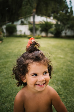 portrait of a young cute cheerful little girl with a parrot on top of her head