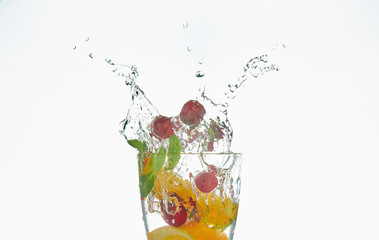 orange splashing into a glass of water with mint and berries on a white background. refreshing summer drink with citrus.