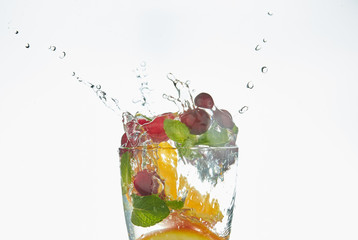 orange splashing into a glass of water with mint and berries on a white background. refreshing summer drink with citrus.