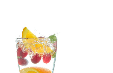 orange splashing into a glass of water with mint and berries on a white background. refreshing summer drink with citrus.