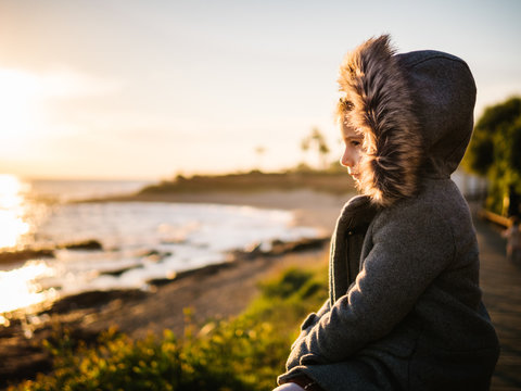 Side view of girl in jacket sitting on beach