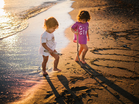 small cute girls drawing on sand with a stick at sunset by the sea shore