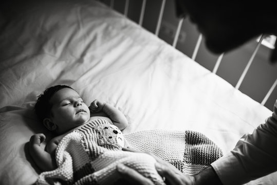 Black and white crop man bending over crib and touching sleeping baby gently in cozy nursery at home
