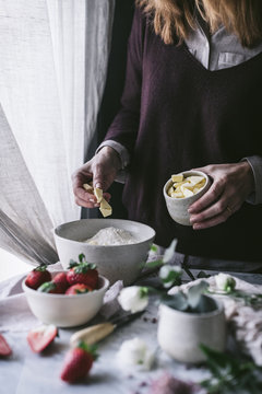 Unrecognizable female adding butter to flour while standing near table and cooking yummy strawberry pastry in kitchen