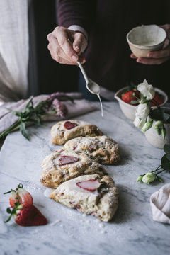 Unrecognizable person adding sweet cream sauce to tasty strawberry scones while cooking in kitchen