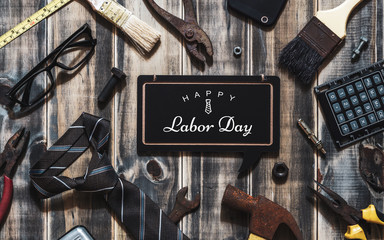 Happy Labor day background concept. Flat lay of construction blue collar handy tools and white collar's accessories over wooden background with text Happy Labor day on black chalkboard.