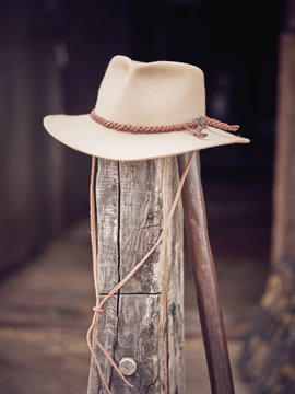 Traditional cowboy hat placed on top of shabby lumber stake on blurred background of stable on ranch