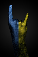 A hand with a drawn Ukraine flag shows a goat sign on a dark background