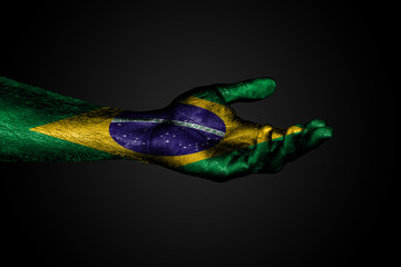 Obraz na płótnie Canvas Outstretched hand with a drawn Brazil flag, a sign of help or a request, on a dark background.