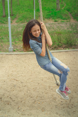 Smiling girl riding around on rope Charming cheerful brunette girl with eyes closed riding around on rope on playground in park