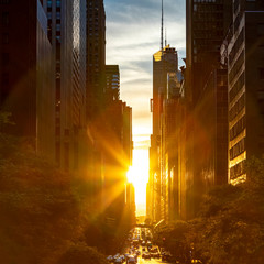 Rays of sunlight shining between the skyline buildings along 42nd Street in Midtown Manhattan, New...