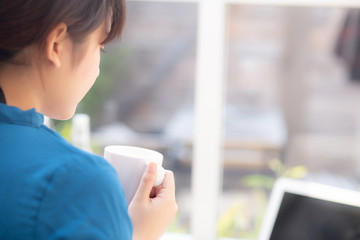 Fototapeta premium Beautiful young freelance asian woman working and on laptop computer at desk coffee shop with professional, asia girl using notebook and drink coffee, business and lifestyle concept, back view.
