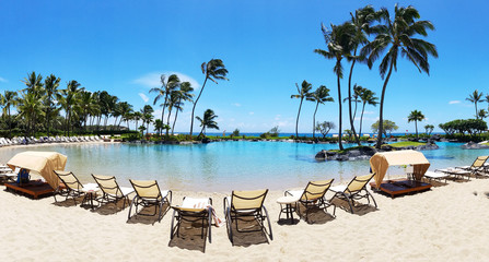 Tropical paradise scene with beach chairs lined up around a swimming pool in Hawaii