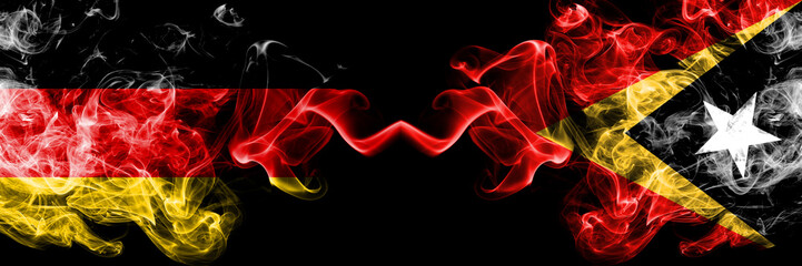 Germany vs East Timor smoky mystic flags placed side by side. Thick colored silky smoke flags of Deutschland and East Timor