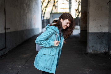 Cheerful girl in a blue jacket among dirty old city walls.