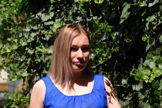 Portrait of a girl in a blue dress on a background of green arbor of ivy.
