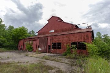 Large red abandoned building with cloudy sky and overgrown brush