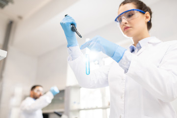 Below view of concentrated young woman in white coat and rubber gloves using dropper while mixing...