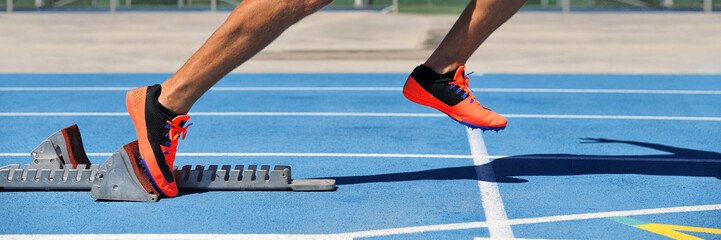Track spikes shoes feet on starting blocks on running track and field stadium blue lanes. Sprinting...