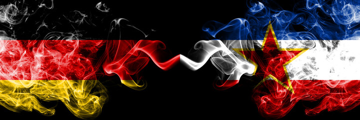 Germany vs Yugoslavia smoky mystic flags placed side by side. Thick colored silky smoke flags of Deutschland and Yugoslavia