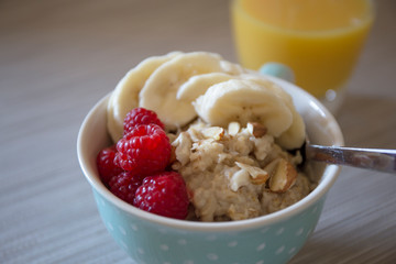 Bowl of homemade oatmeal porridge with banana, raspberry and almonds