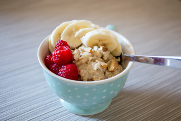 Bowl of homemade oatmeal porridge with banana, raspberry and almonds