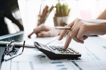 Close up Business woman using calculator and laptop for do math finance on wooden desk in office...