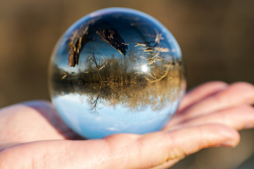 Woman's hand holding Clear Quartz Sphere reflecting lake, forest and sky.