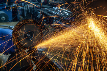 Close-up of a man sawing   bearing metal with a hand circular saw, bright flashes flying in different directions, in the background tools for an auto repair shop. Work of auto mechanics.