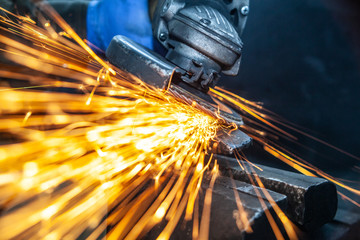 Close-up of a man sawing   bearing metal  hammer with a hand circular saw, bright flashes flying in different directions, in the background tools for an auto repair shop. Work of auto mechanics.