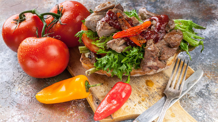 Close Up grilled meat on a traditional chabbata with sweet peppers, tomatoes and herbs on a cutting board.