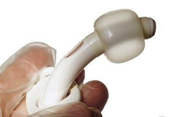 Adult tracheostomic cannula with inflated ballon with visible suction port hole, held in hand in latex glove, white background