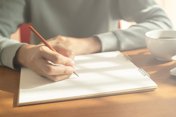 hands woman writing notebook. On wooden desk background have coffee cup and laptop in morning ...