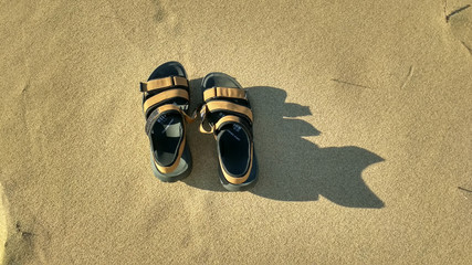 Pair of sandals on the sand. Contrast shadow on the sand.