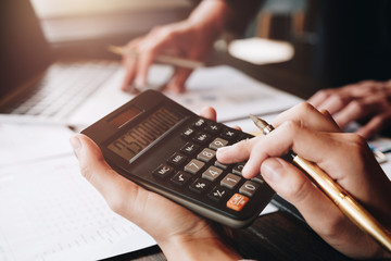 Close up Businessman and partner using calculator and laptop for calaulating finance, tax, accounting, statistics and analytic research concept