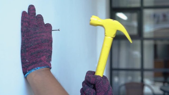 Close up hands with gloves hammering a nail to living room wall