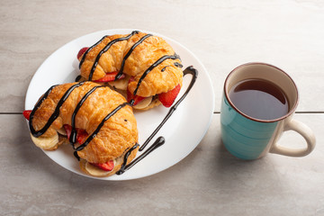 fresh croissant on the table, with hot tea, strawberries and bananas, delicious breakfast